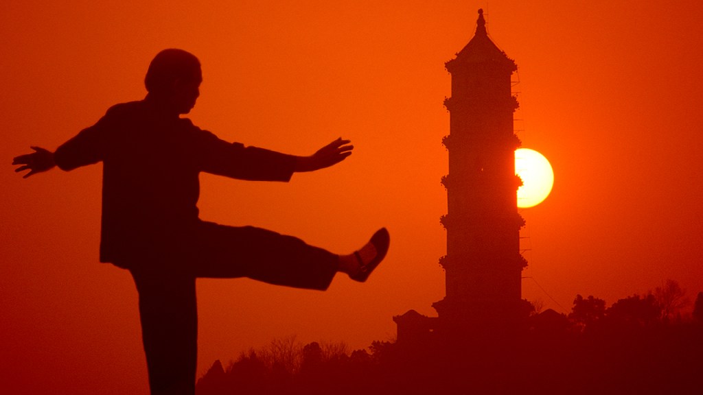 Older lady doing Tai Chi exercising at sunset.