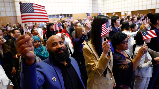 About 200 people wave American flags after being sworn in at a naturalization ceremony in Boston on April 17, 2024. (Danielle Parhizkaran/The Boston Globe via Getty Images)