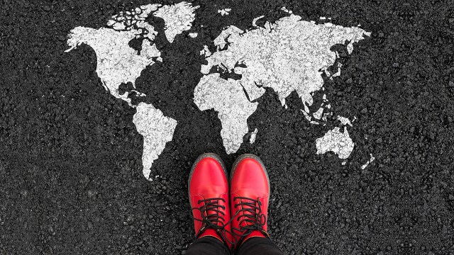 World map on an asphalt with person in red shoes standing next to it