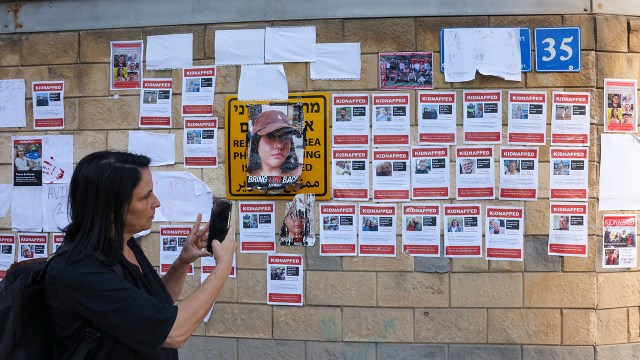 A woman photographs a poster showing Israeli hostages held by Hamas on the exterior wall of the Ministry of Defense in Tel Aviv on October 16, 2023. (Ahmad Gharabri/AFP via Getty Images)