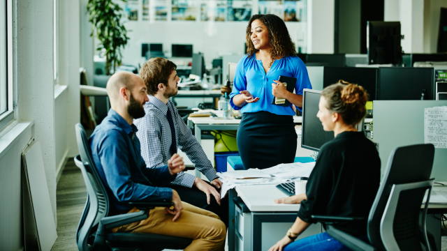 Businesswoman leading informal meeting with colleagues at office workstation.